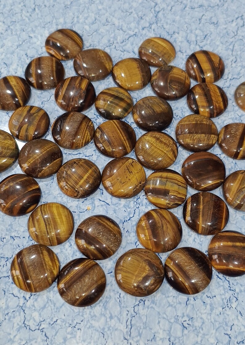 May include: A collection of round, polished tiger's eye stones. The stones are a mix of brown, gold, and black colors with a shimmering, iridescent effect.