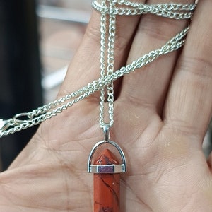 May include: A silver chain necklace with a red jasper point pendant. The pendant is held in a silver setting with a small silver loop at the top.