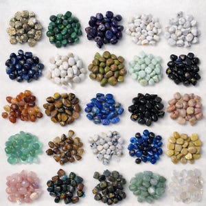 May include: A selection of polished gemstones in diverse colours, such as green, blue, white, and brown. The stones are arranged in small, neat piles, displaying their natural textures and hues. The image is well-lit, highlighting the details of each stone.