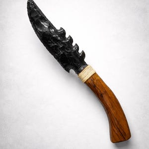 May include: A handcrafted obsidian knife with a serrated blade and a curved wooden handle. The handle is wrapped with a natural fiber cord. The knife is a dark, glossy black with a warm brown handle.