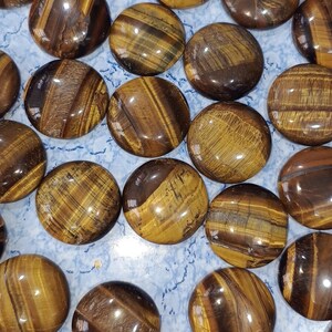 May include: A collection of polished tiger's eye stones, each with a unique pattern of brown, gold, and black stripes. The stones are smooth and glossy, with a slightly rounded shape.