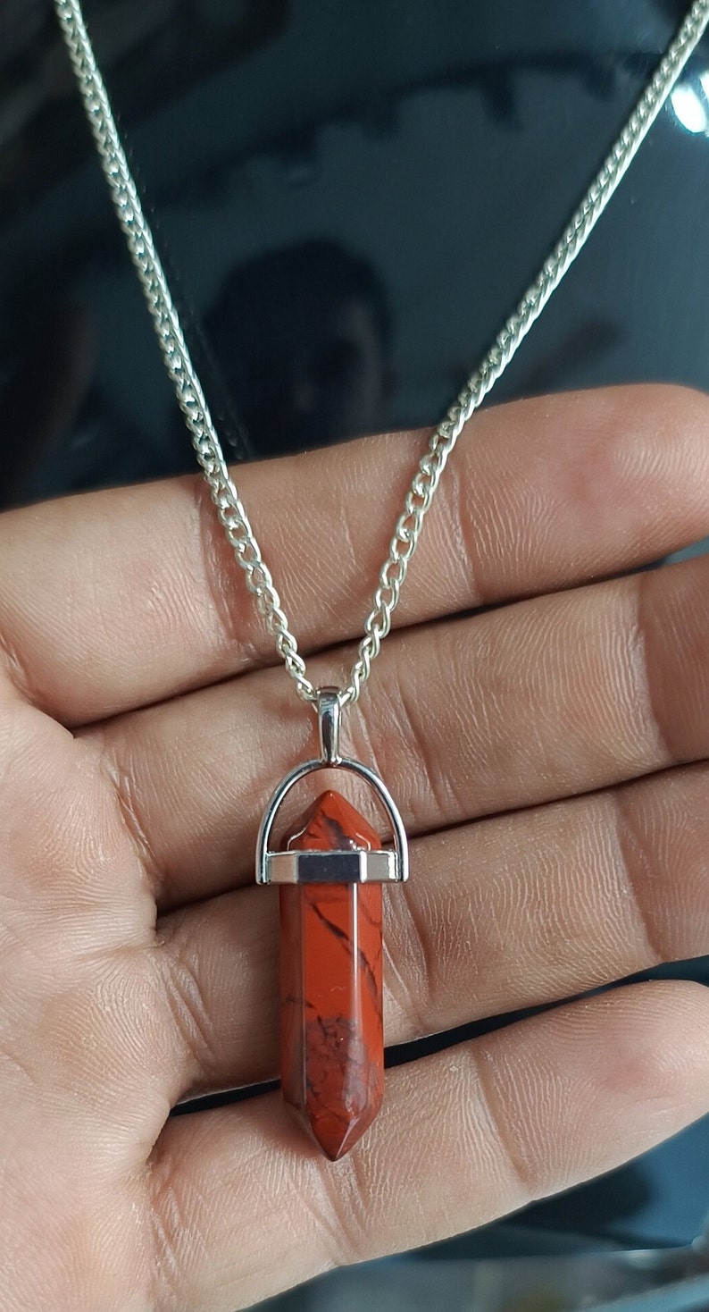 May include: A silver chain necklace with a red jasper point pendant. The pendant is set in a silver bezel and has a silver bail.