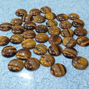 May include: A collection of tiger's eye cabochons, each with a unique pattern of brown and gold stripes. The cabochons are smooth and polished, with a glossy finish.