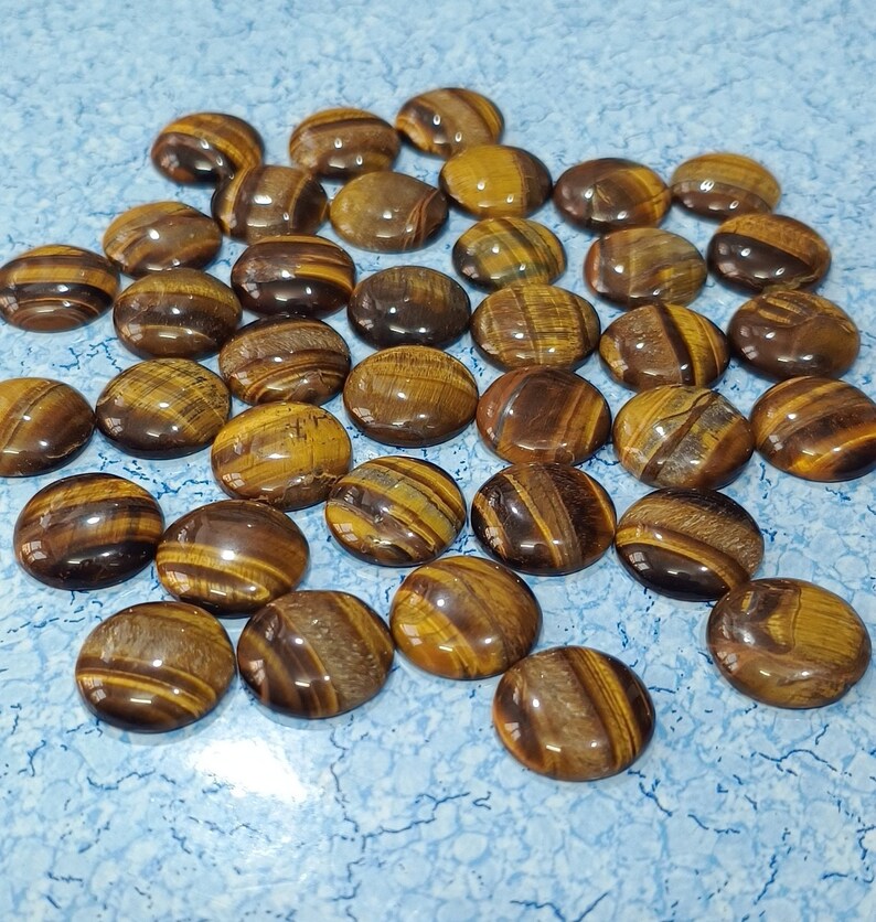 May include: A collection of tiger's eye cabochons, each with a unique pattern of brown and gold stripes. The cabochons are smooth and polished, with a glossy finish.