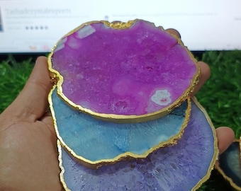 May include: Three agate coasters with gold trim. The coasters are stacked on top of each other. The top coaster is pink, the middle coaster is blue, and the bottom coaster is purple.