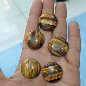 May include: Five round, polished tiger's eye stones with brown and gold stripes. The stones are smooth and have a glossy finish.