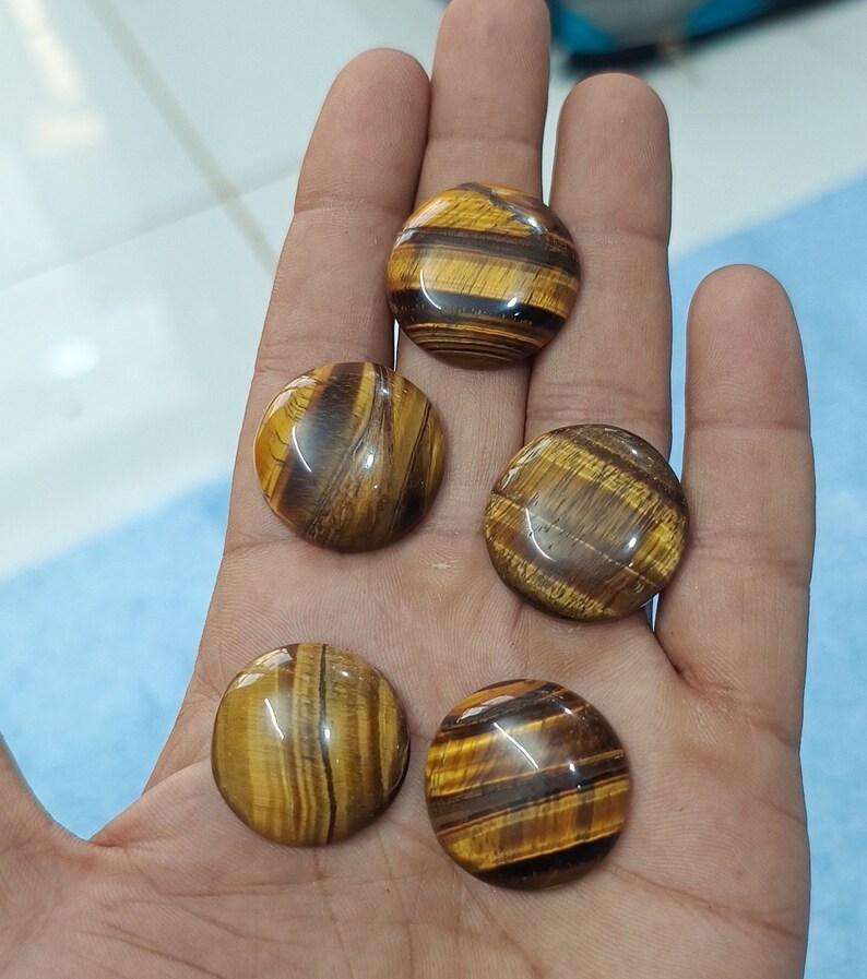May include: Five round, polished tiger's eye stones with brown and gold stripes. The stones are smooth and have a glossy finish.