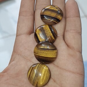 May include: Four round, polished tiger's eye stones in shades of brown and gold. The stones are arranged in a row, with the largest stone at the top and the smallest stone at the bottom.