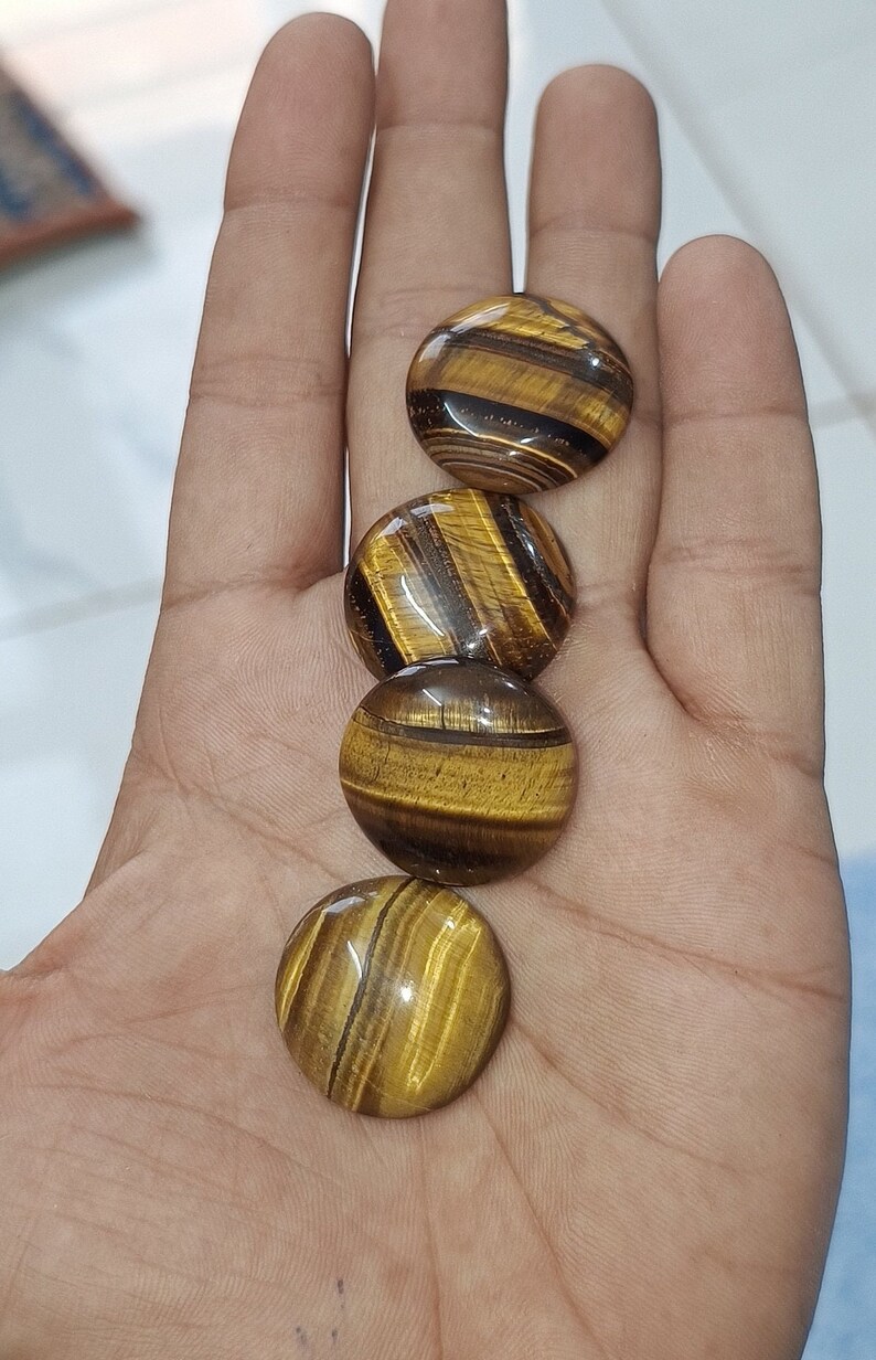 May include: Four round, polished tiger's eye stones in shades of brown and gold. The stones are arranged in a row, with the largest stone at the top and the smallest stone at the bottom.