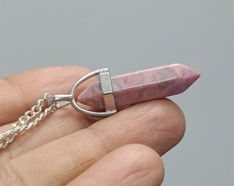 May include: A silver chain necklace with a pink and gray crystal pendant. The pendant is a pointed crystal with a silver setting.