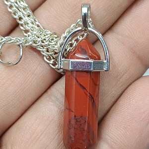 May include: A silver chain necklace with a red gemstone pendant. The pendant is a pointed, faceted crystal with a silver setting.