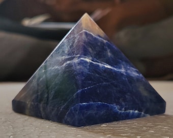 May include: A blue and white lapis lazuli pyramid crystal. The crystal is smooth and polished, with a natural, striated pattern.