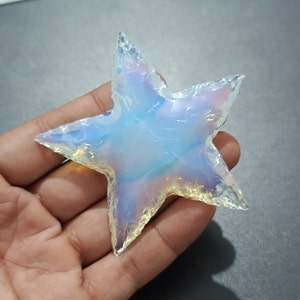 May include: A star-shaped piece of iridescent opal, with a blue and white color scheme. The opal is translucent and has a smooth, polished surface.