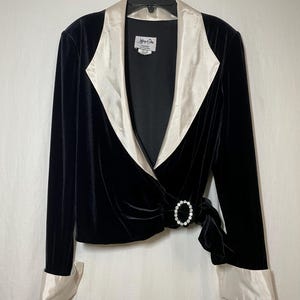 May include: A black velvet wrap jacket with a white satin collar and cuffs. The jacket has a rhinestone buckle at the waist.
