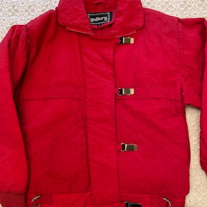 May include: A bright red jacket with a high collar and gold-colored metal clasps. The jacket has a quilted texture and features the brand name "gallery" on a small label near the collar. The cuffs are ribbed, and there are metal rings at the bottom.