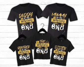 Könnte beinhalten: Vier schwarze T-Shirts mit goldfarbenem Text und Grafiken. Die Shirts sagen "Daddy of the Notorious One", "Mommy of the Notorious One", "Brother of the Notorious One" und "Sister of the Notorious One".