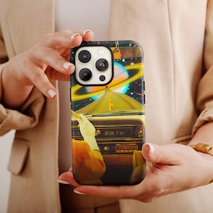 Può includere: Una custodia per telefono con un design a collage in stile retrò che presenta un'auto che guida attraverso una galassia con un pianeta e stelle. La custodia ha un bordo nero e un obiettivo della fotocamera trasparente.