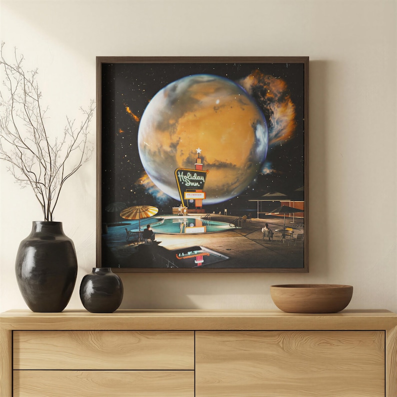 May include: A square framed wall art print depicting a surreal scene of a Holiday Inn sign and a swimming pool set against a large, glowing orange planet in deep space. The artwork features a dark night sky, a pool with umbrellas, and a planet.