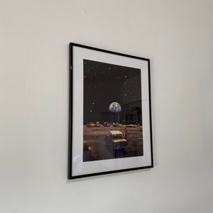 May include: A framed print of a surreal scene with a car driving on a road with a planet Earth in the sky. The scene is set against a black background with stars.