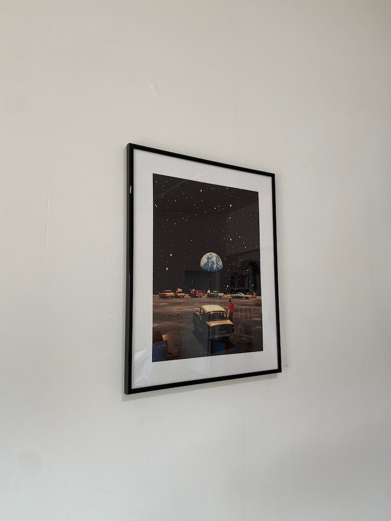 May include: A framed print of a surreal scene with a car driving on a road with a planet Earth in the sky. The scene is set against a black background with stars.