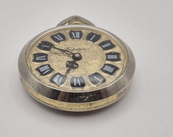 May include: A silver and gold Trafalgar pocket watch with a gold-tone face. The watch features black Roman numerals and hands, with the word "Trafalgar" printed on the face. The watch is a classic timepiece.