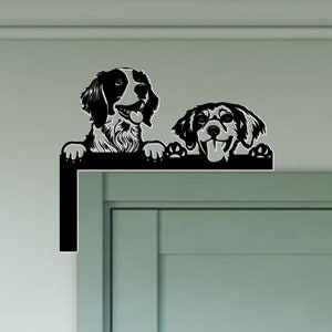 May include: Black silhouette of two dogs peeking over a fence. The dogs are looking at the camera with their tongues out. The image is a cutout design.