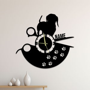 Könnte beinhalten: Schwarze Silhouette Wanduhr mit einem Hund, einer Schere und Pfotenabdrücken. Das Zifferblatt der Uhr ist weiß mit schwarzen Zahlen und Zeigern. Die Uhr ist mit "NAME" beschriftet.