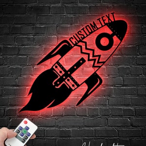 May include: A red neon rocket ship with a black outline and the text "CUSTOM TEXT" above it. The rocket ship is on a brick wall background. A remote control is in the lower left corner of the image.