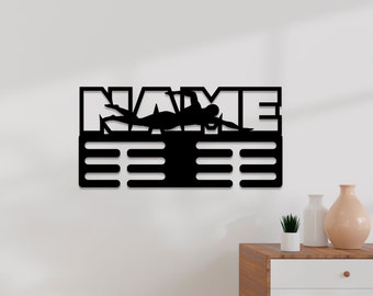 May include: Black metal wall-mounted medal display with the word "NAME" and a silhouette of a swimmer. The display has 10 slots for medals.