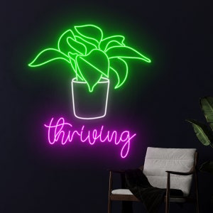 Könnte beinhalten: Neon-Schild mit einer grünen Umrandung einer Topfpflanze und dem Wort "thriving" in pinkfarbenem Neon.