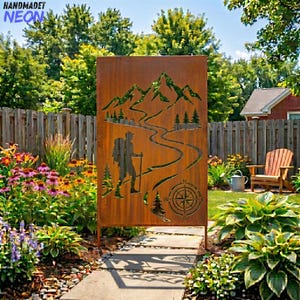 May include: A rusty brown metal garden screen featuring a hiker with a backpack and walking stick, mountains, a winding path, trees, and a compass design. The screen is set in a garden with a wooden fence and lush greenery.