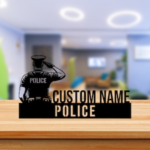Pode incluir: Silhueta preta de um policial a saudar com a palavra "POLICE" no seu uniforme. Abaixo do policial está um retângulo preto com o texto "CUSTOM NAME POLICE".