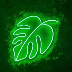 May include: A neon green monstera leaf shaped light, with a white outline, on a green fluffy surface.