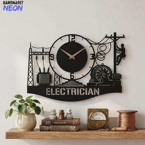 May include: Black metal wall clock with a cutout design featuring an electrician theme. The clock has a circular face with gold-colored hands and the word "ELECTRICIAN" below. The design includes power lines, a transformer, and a lineman.