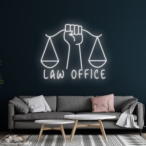 Pode incluir: Uma placa de néon branca que diz "LAW OFFICE" com um punho segurando balanças da justiça. A placa está montada em uma parede azul escura acima de um sofá cinza e duas mesas de centro brancas.