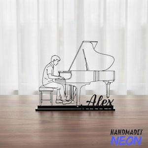 May include: A black metal decorative piece depicting a line drawing of a person playing a grand piano. The name "Alex" is written in cursive below the piano. The words "HANDMADET NEON" are at the bottom.
