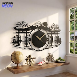 May include: A black wall clock featuring a laser-cut silhouette of Mount Fuji, a torii gate, and cherry blossom branches. The circular clock face has gold-colored hands and numerals at the 12, 3, 6, and 9 positions, mounted on a white wall.