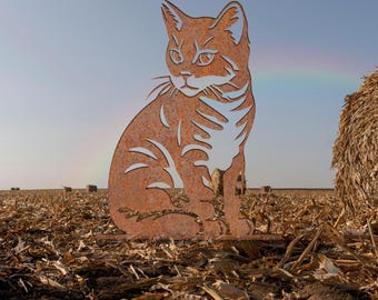 May include: A flat, rust-colored metal silhouette of a sitting cat with cut-out details defining its facial features, ears, and striped fur pattern. The cat figure is positioned upright, displaying a weathered, textured surface finish.