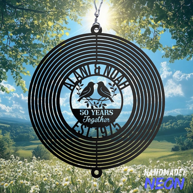 May include: A black metal wind spinner with a circular design. The center features the names "ALANI & NOAH", two birds, and the text "50 YEARS Together EST 1975". The spinner hangs from a silver hook, with a scenic background.