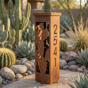 Puede incluir: Un poste de dirección alto y rectangular de metal color óxido, con un diseño de cactus cortado con láser en el panel frontal y los números de casa 2541 cortados verticalmente en el lado derecho, apoyado sobre una base plana.