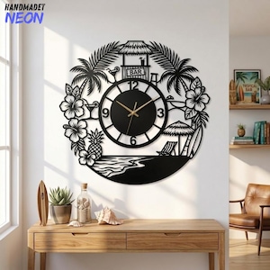 Puede incluir: Un reloj de pared circular negro con una escena de playa tropical que incluye palmeras, flores de hibisco, una piña, un bar tiki y una tabla de surf. La esfera es negra con manecillas doradas y los números blancos 3, 6, 9 y 12.