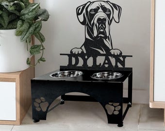 May include: Black metal dog bowl stand with two bowls. The stand features a silhouette of a Great Dane dog with the name "DYLAN" underneath. The stand has paw prints on the bottom.