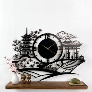 May include: Black metal wall clock with a Japanese landscape design. The clock features a pagoda, koi fish, cherry blossoms, and a mountain scene. The clock hands are gold-colored.