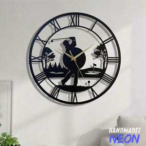 May include: Black metal golf-themed wall clock with Roman numerals. The clock features a silhouette of a golfer mid-swing, with a golf course scene in the background. The clock hands are gold.