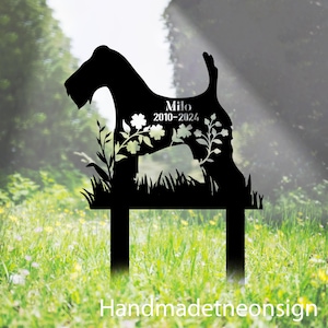 May include: A black metal garden stake featuring the silhouette of a terrier dog. The design includes cut-out floral patterns and the text "Milo" followed by the years "2010-2024" engraved in the center of the dog's body shape.