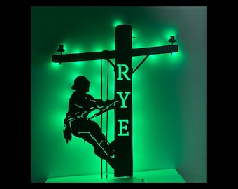 May include: A black metal silhouette of a person climbing a utility pole with the name "RYE" on the pole. The silhouette is lit with green lights.