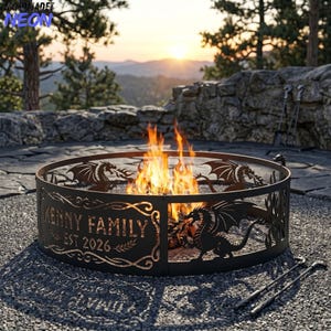 May include: A circular black metal fire pit ring featuring laser-cut dragon silhouettes and decorative scrollwork. The text "KENNY FAMILY" and "EST 2026" is cut into the front panel. Bright orange flames burn inside the ring on a gravel surface.