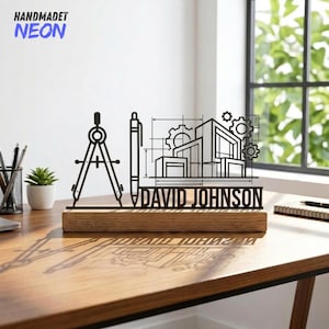 Puede incluir: Un diseño arquitectónico negro con un compás, un bolígrafo, un contorno de edificio y engranajes, montado sobre una base de madera. El nombre "DAVID JOHNSON" se muestra debajo. Las palabras "HANDMADET NEON" están en la esquina superior izquierda.