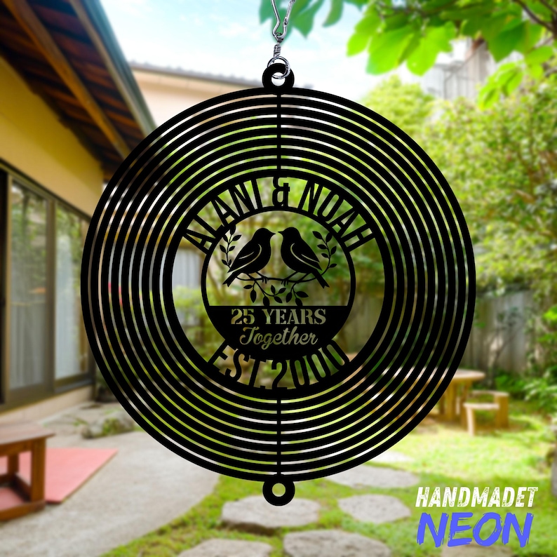 Pode incluir: Moinho de vento de metal preto com um design circular. O centro apresenta os nomes "ALANI & NOAH", dois p&aacute;ssaros e o texto "25 YEARS Together EST 2000". O canto inferior direito tem o texto "HANDMADET NEON".