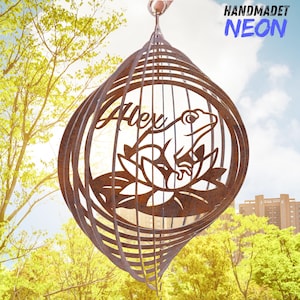May include: A brown metal wind spinner with a frog design and the name "Alex". The spinner is suspended from a metal hook and features the text "HANDMADET NEON". The design includes a frog on a lily pad.